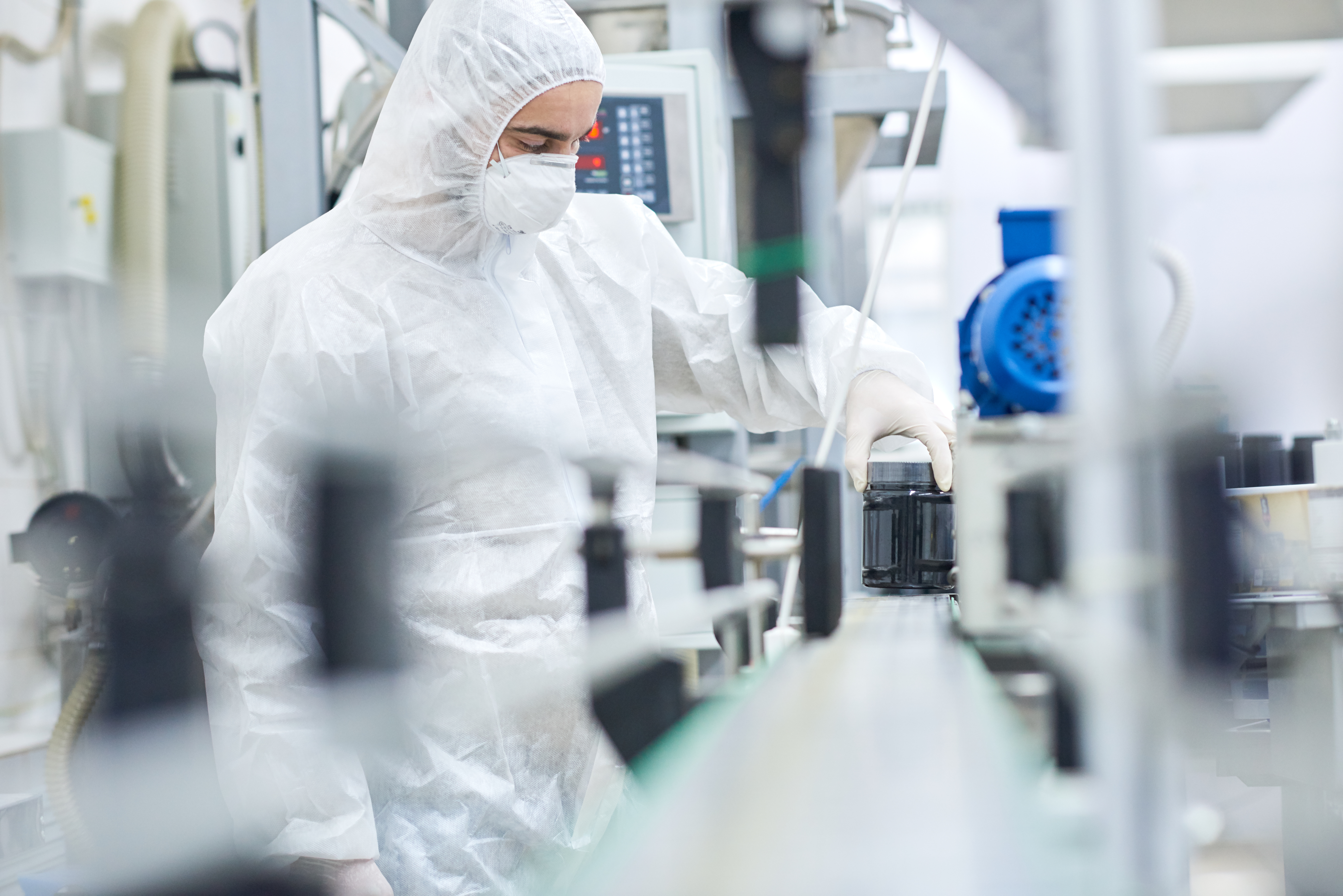 Operator in cleanroom apparel finishing a supplement bottle on a packaging line